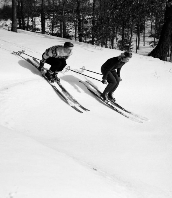 Молодая пара на лыжах мчится вниз по склону в традиционных лыжных ботинках на шнуровке